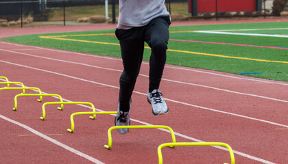 Fototapeta premium Runner in air over small plastic hurdels running a sports drill in lane on a track
