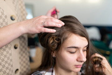Fototapeta premium The stylist curls the girl's hair with a curling iron