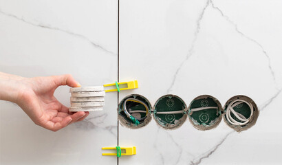 Drilled holes for sockets in the master's hand against the background of porcelain tiles. Repair in...