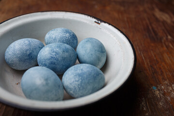 Easter eggs painted blue in white bowl on brown wooden background. Close up shot