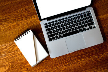 Top view of open school notebook with blank pages, mock up laptop, glass od water and pencil on wood table background. Flat lay, creative workspace office. Business-education concept with copy space. 