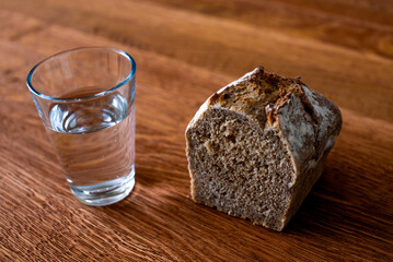 A glass of water and a loaf of bread on a wooden table. Fasting for bread and water to strengthen the spirit. Lent. Easter. Prison food. Food for poor.