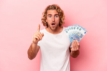Young caucasian man holding banknotes isolated on pink background having an idea, inspiration concept.