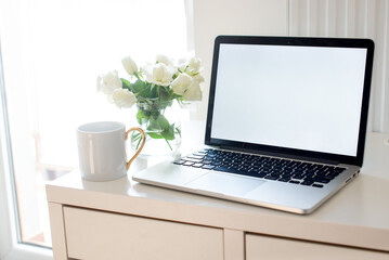 Laptop with white blank screen on white work table. White interior home office concept. Female...