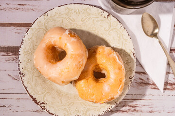 Donuts covered with white icing on a vintage plate on an old wooden table. Aerial view, horizontal orientation. Homemade food concept.