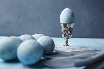 Beautiful painted easter eggs and silver feathers on blue background. One Easter egg in egg cup. Close up shot