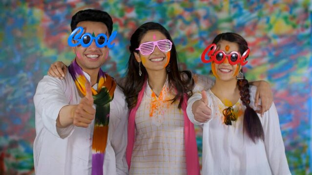 Two Indian youngsters wearing cool sunglasses doing a thumbs-up gesture - Holi festival  best friends  holi party. A young man and two females embrace each other while looking at the camera - leisu...