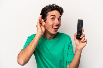 Young caucasian man holding a tv remote isolated on white background trying to listening a gossip.