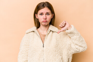 Young English woman isolated on beige background showing a dislike gesture, thumbs down....