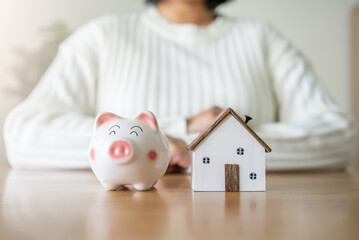 Woman with piggy bank and future house concept of saving and loan money for house. To rent or buy new house with saving money in piggy bank.