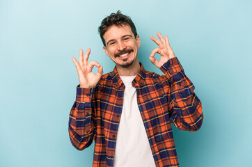 Naklejka premium Young caucasian man isolated on blue background cheerful and confident showing ok gesture.