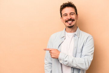 Young caucasian man isolated on beige background smiling and pointing aside, showing something at blank space.