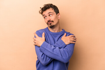 Young caucasian man isolated on beige background hugs, smiling carefree and happy.