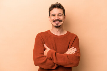 Young caucasian man isolated on beige background who feels confident, crossing arms with determination.