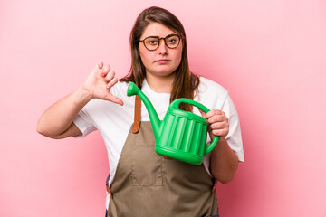Young gardener caucasian overweight woman holding watering can isolated background showing a dislike gesture, thumbs down. Disagreement concept.