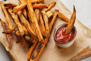 Healthy homemade oven baked sweet potato fries on a baking parchment, wooden board, with ketchup sauce