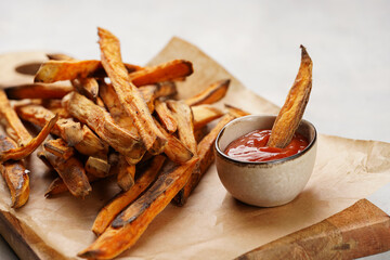 Healthy homemade oven baked sweet potato fries on a baking parchment, wooden board, with ketchup sauce