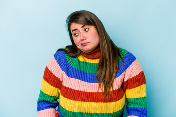 Young caucasian overweight woman isolated on blue background shrugs shoulders and open eyes...