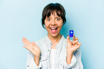 Young hispanic woman holding a batterie isolated on blue background surprised and shocked.