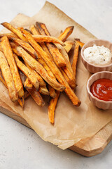 Healthy homemade oven baked sweet potato fries on a baking parchment, wooden board, with ketchup sauce and mayonnaise