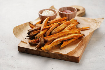 Healthy homemade oven baked sweet potato fries on a baking parchment, wooden board, with ketchup...