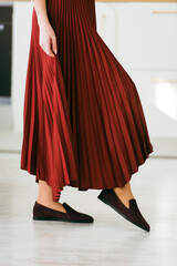 Photo of women's legs in a stylish suede burgundy loafers. Woman wearing red skirt.