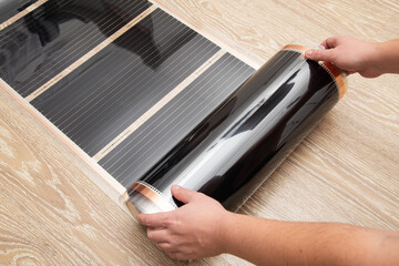A man rolls out a roll of infrared floor heating for installation. Close-up, comfortable