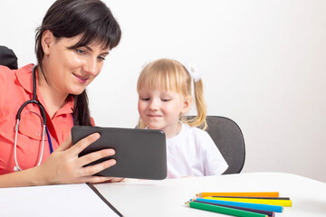 Doctor pediatrician shows a tablet to a little girl. Treatment of children. Copy space for text