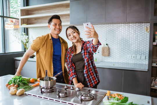asian couple taking selfie while cooking together in the kitchen