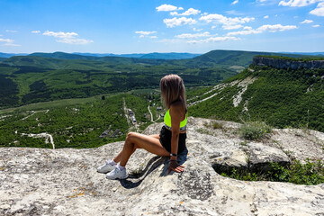 A girl on the background of a view of the Crimean mountains from the cave city of Tepe-Kermen. May 2021. Crimea. Russia.