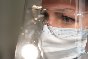 Young woman doctor or nurse working. Girl in medical mask, glasses and shield.