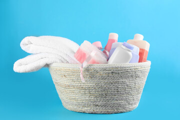 Wicker basket full of different baby cosmetic products and bathing accessories on light blue background