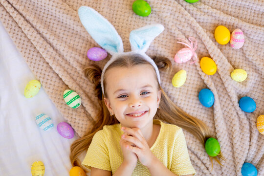 easter, a little child girl among painted colored eggs is preparing for the holiday smiling and having fun, top view