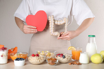 Woman holding paper heart and large intestine model near table with food, closeup. Balanced...