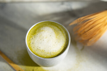 Organic green matcha tea with milk. Matcha powder and tea drink in a bowl. Chasen bamboo whisk for brewing matcha tea top view on white background with beautiful shades. Copy space.
