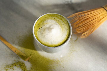 Organic green matcha tea with milk. Matcha powder and tea drink in a bowl. Chasen bamboo whisk for brewing matcha tea top view on white background with beautiful shades. Copy space.