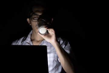 Low light view. A man drink milk while using a laptop. He work online at home late at night.
