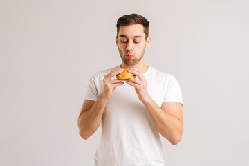 Portrait of hungry young man with enjoying eating delicious burger on white isolated background....