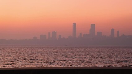 Real time close up view of Mumbai City Skyline as seen from famous tourist destination Marine Drive during golden hour. Silhouette shot of buildings during sunset. Bombay, Maharashtra, India. 4897.