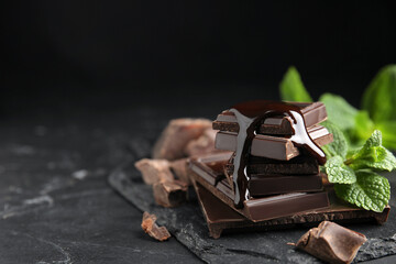 Tasty chocolate pieces with syrup and mint on black table. Space for text