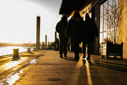 Sunset with three people walking towards it, next to a sea channel.