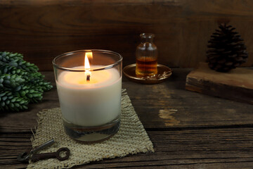 the burning luxury aromatic scented candle glass on the wooden table with background of vintage wooden wall of the cottage in the living room to creat relax ambient during christmas party celebration