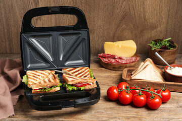 Modern grill maker with sandwiches and different products on wooden table