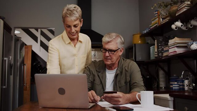 Caucasian mature couple sitting in kitchen on laptop 