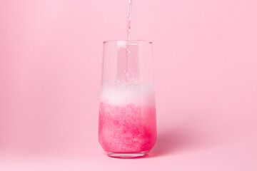 A pink drink is poured into a glass on a pink background. Carbonated sweet water. delicious drink