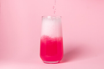 A pink drink is poured into a glass on a pink background. Carbonated sweet water. delicious drink