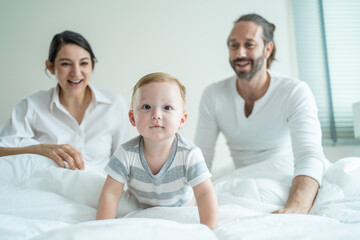 Caucasian loving parents play with baby boy child on bed in bedroom. 