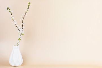 White vase with twigs of blossoming spring tree branch on beige background with copy space. Minimal...