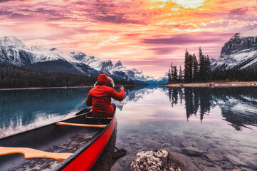 Male traveler in winter coat rowing a red canoe in Spirit Island on Maligne Lake at the sunset - obrazy, fototapety, plakaty