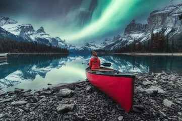Aurora borealis over Spirit island with female traveler sitting on red canoe on Maligne Lake at...